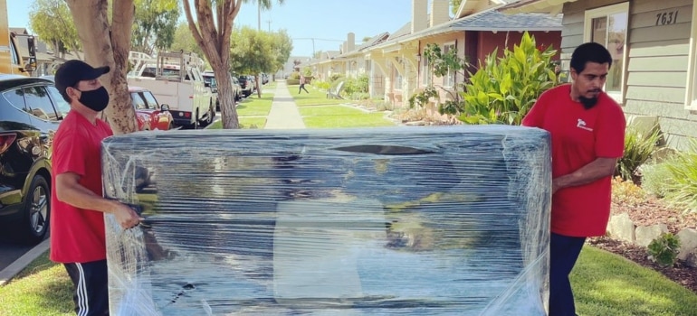 Movers moving a wrapped couch - one of the traits of reliable Los Angeles movers is packing properly