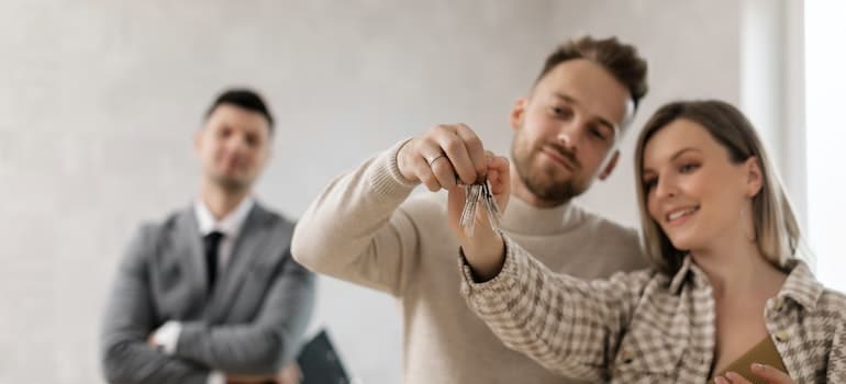 A couple holding house keys, standing next to a realtor